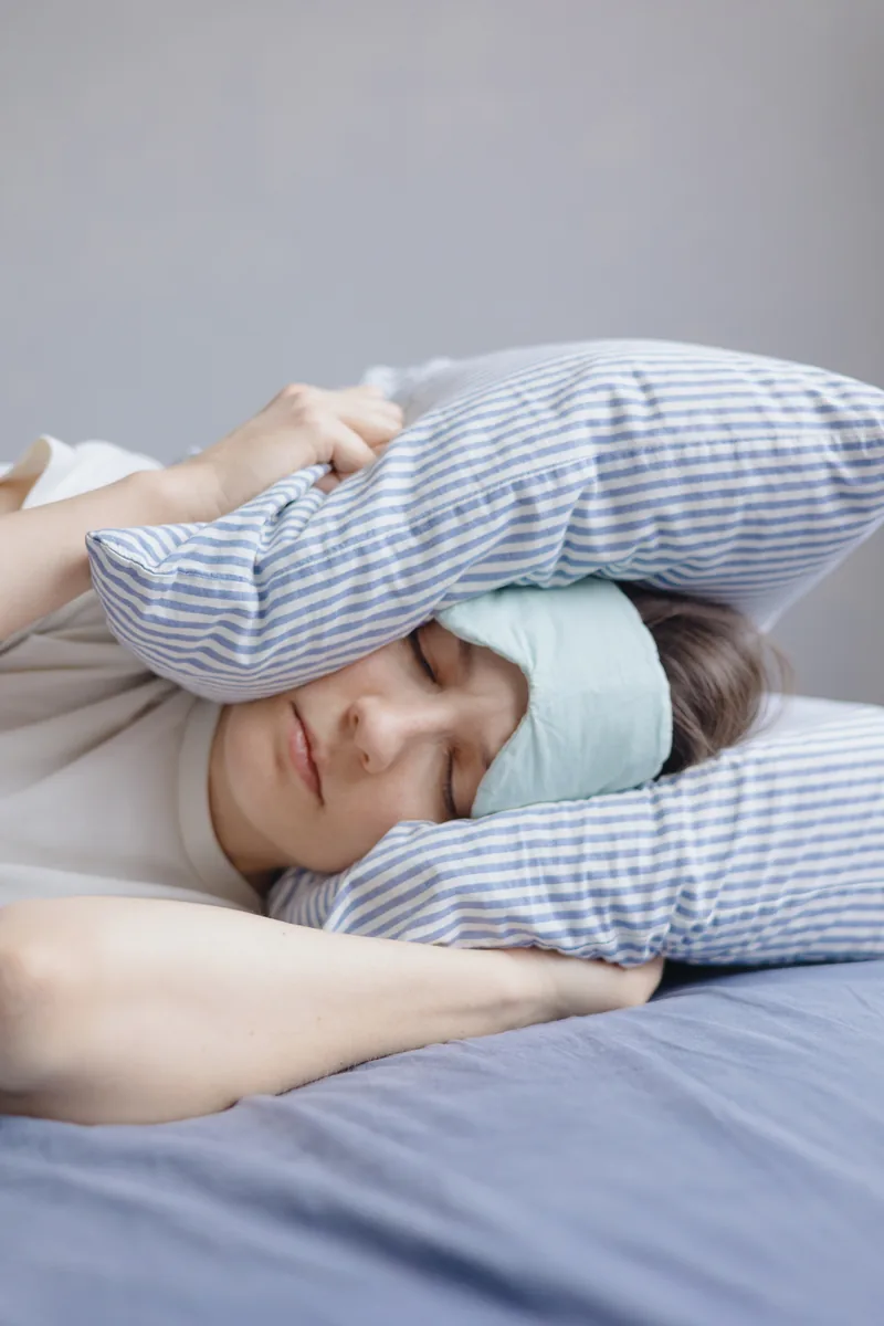 Femme au lit avec un masque de nuit, illustrant les troubles du sommeil liés au stress